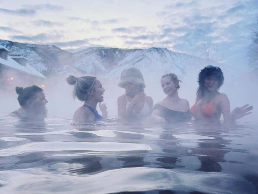 Five women enjoying the Grand Pool in the winter with mountains behind them at Glenwood Hot Springs Resort